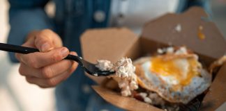 Close-up of a sunny side up egg in a takeout box being eaten with a fork.