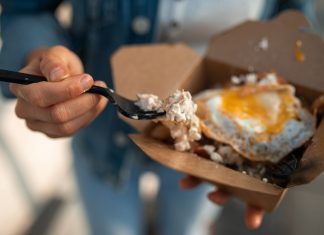 Close-up of a sunny side up egg in a takeout box being eaten with a fork.