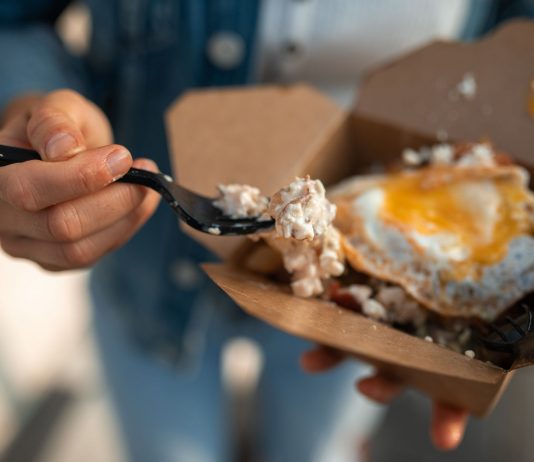 Close-up of a sunny side up egg in a takeout box being eaten with a fork.