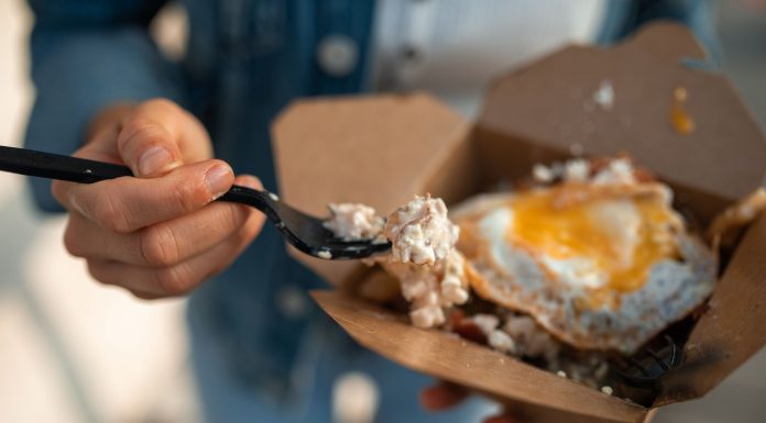 Close-up of a sunny side up egg in a takeout box being eaten with a fork.