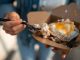 Close-up of a sunny side up egg in a takeout box being eaten with a fork.