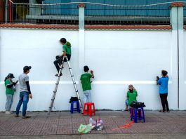 Downtown Church Members Trade Pews for Paintbrushes to Help Neighbors Group of artists painting a mural on a public wall outdoors using ladders and stools.
