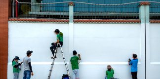 Downtown Church Members Trade Pews for Paintbrushes to Help Neighbors Group of artists painting a mural on a public wall outdoors using ladders and stools.
