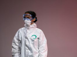 Medical professional in full protective suit with goggles and mask, studio setting.