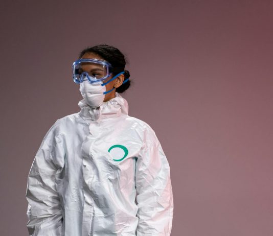 Medical professional in full protective suit with goggles and mask, studio setting.