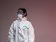 Medical professional in full protective suit with goggles and mask, studio setting.