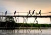 Unrecognizable active ethnic kids jogging on footbridge above lake while working out under sunset sky
