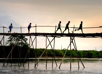 Film Screening in Jersey City Tells the Story of Teenage Migrants Unrecognizable active ethnic kids jogging on footbridge above lake while working out under sunset sky