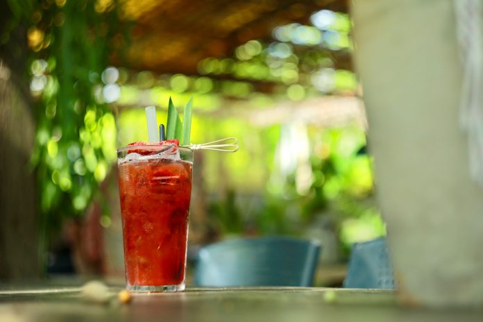 A vibrant strawberry cocktail with pineapple garnish on an outdoor table in sunny garden.