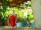 A vibrant strawberry cocktail with pineapple garnish on an outdoor table in sunny garden.