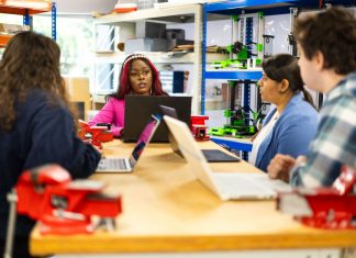 Diverse group of students engaged in a collaborative technical class discussion in a workshop setting.