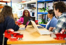Diverse group of students engaged in a collaborative technical class discussion in a workshop setting.