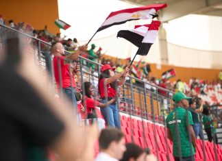 Soccer fans in the stadium wave Egyptian flags, showing their support during a lively sports match.