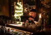 Young man enjoying a drink in a cozy bar with Christmas lights and decor.