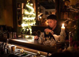 Hoboken’s The Waiting Room Hosts Xmas in July Event Young man enjoying a drink in a cozy bar with Christmas lights and decor.