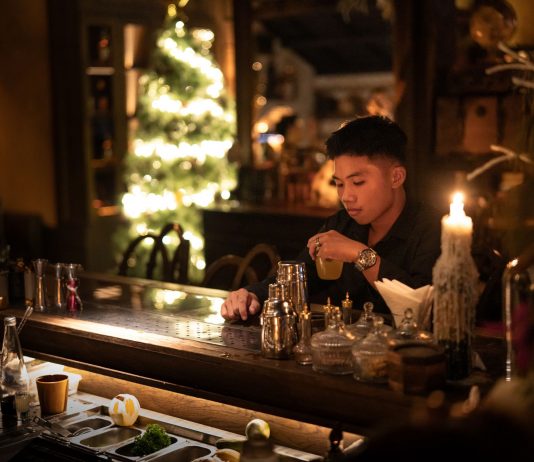 Young man enjoying a drink in a cozy bar with Christmas lights and decor.