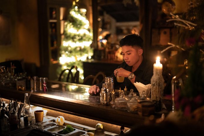 Young man enjoying a drink in a cozy bar with Christmas lights and decor.
