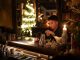 Hoboken’s The Waiting Room Hosts Xmas in July Event Young man enjoying a drink in a cozy bar with Christmas lights and decor.
