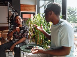 Hoboken’s Third Spaces Feel Lonely? Here’s the Real Solution Two friends having a lively conversation over coffee in a cozy coffee shop setting.