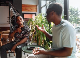 Hoboken’s Third Spaces Feel Lonely? Here’s the Real Solution Two friends having a lively conversation over coffee in a cozy coffee shop setting.