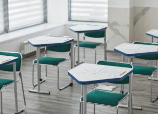An empty classroom with arranged desks, exam papers, and pencils ready for students.