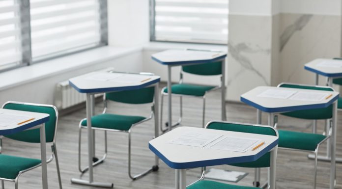 An empty classroom with arranged desks, exam papers, and pencils ready for students.