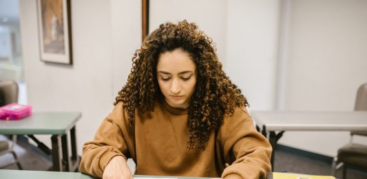 Young woman studying for an exam in a college classroom with books and notes.
