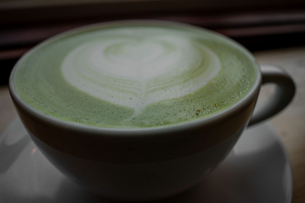 Close-up of a frothy matcha latte with heart latte art in a ceramic cup, warm and inviting.