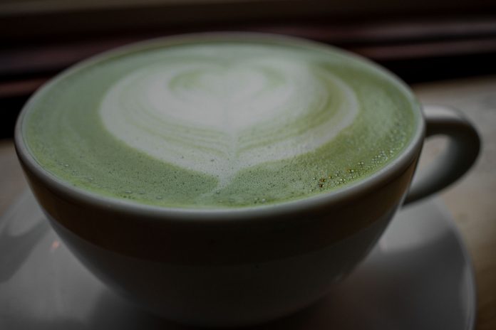 Close-up of a frothy matcha latte with heart latte art in a ceramic cup, warm and inviting.