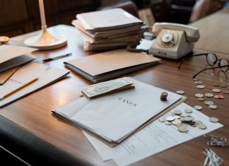 Jersey City Budget Gap Narrows, But Tax Hike Question Lingers Close-up of an office desk with tax documents, coins, glasses, and an old phone, symbolizing finance and organization.