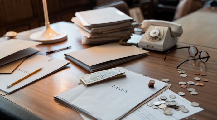 Close-up of an office desk with tax documents, coins, glasses, and an old phone, symbolizing finance and organization.