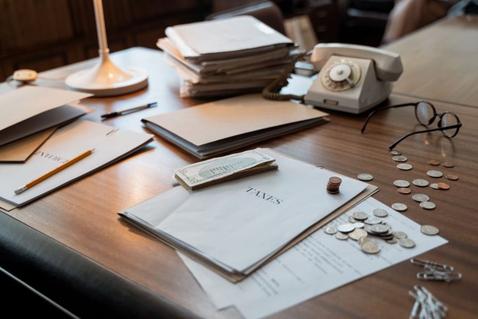 jersey-city-budget-gap-narrows-but-tax-hike-questi Close-up of an office desk with tax documents, coins, glasses, and an old phone, symbolizing finance and organization.