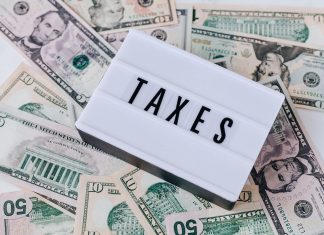 Jersey City Council Votes to Use Cannabis Tax Revenue to Plug Budget Gap From above of white retro lightbox with TAXES inscription placed on pile of USA dollar bills on white surface
