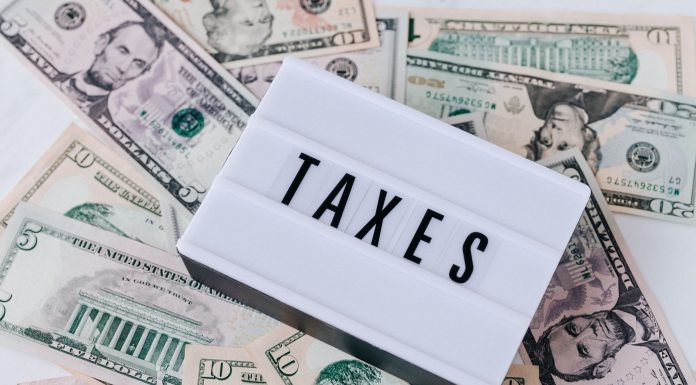 From above of white retro lightbox with TAXES inscription placed on pile of USA dollar bills on white surface