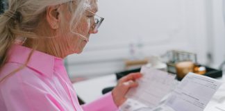 Elderly woman in a pink shirt reviewing paperwork at home.