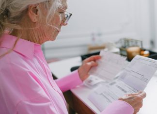 Elderly woman in a pink shirt reviewing paperwork at home.