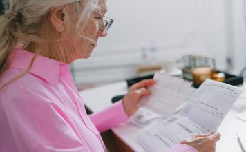 Elderly woman in a pink shirt reviewing paperwork at home.