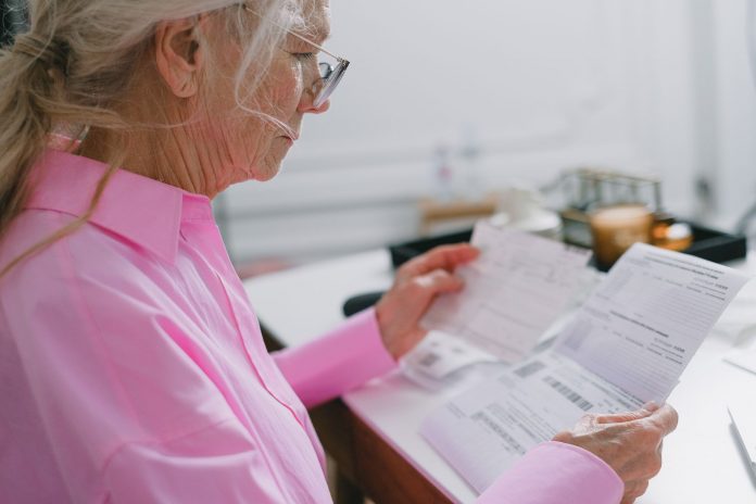 Elderly woman in a pink shirt reviewing paperwork at home.