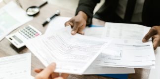 Two professionals exchanging documents in an office setting, focusing on paperwork and data analysis.