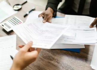 Jersey City launches ‘Senior Freeze’ campaign to help seniors save on property taxes Two professionals exchanging documents in an office setting, focusing on paperwork and data analysis.