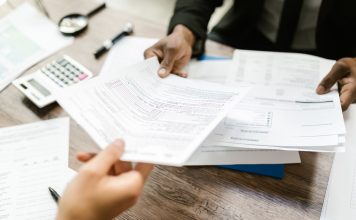 Jersey City launches ‘Senior Freeze’ campaign to help seniors save on property taxes Two professionals exchanging documents in an office setting, focusing on paperwork and data analysis.