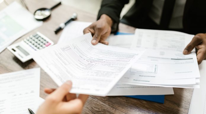 Jersey City launches ‘Senior Freeze’ campaign to help seniors save on property taxes Two professionals exchanging documents in an office setting, focusing on paperwork and data analysis.