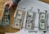Person holds US dollars over financial papers, showing income or budget analysis.