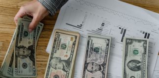 Person holds US dollars over financial papers, showing income or budget analysis.