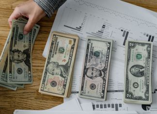 Jersey City must pay $109M in unpaid bills from prior administration, report says Person holds US dollars over financial papers, showing income or budget analysis.