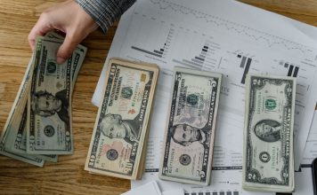 Person holds US dollars over financial papers, showing income or budget analysis.