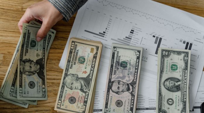 Jersey City must pay $109M in unpaid bills from prior administration, report says Person holds US dollars over financial papers, showing income or budget analysis.