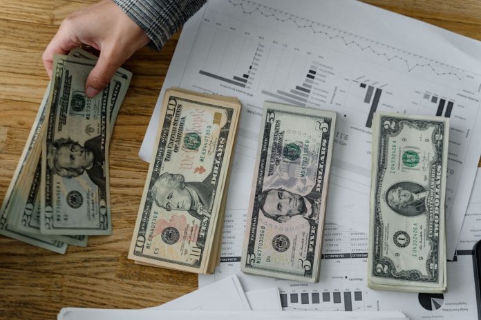 jersey-city-must-pay-109m-in-unpaid-bills-from-pri Person holds US dollars over financial papers, showing income or budget analysis.