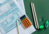 Flat lay of tax forms, calculator, pencils, and clips on green surface, ideal for finance or accounting themes.