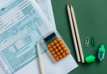 Flat lay of tax forms, calculator, pencils, and clips on green surface, ideal for finance or accounting themes.
